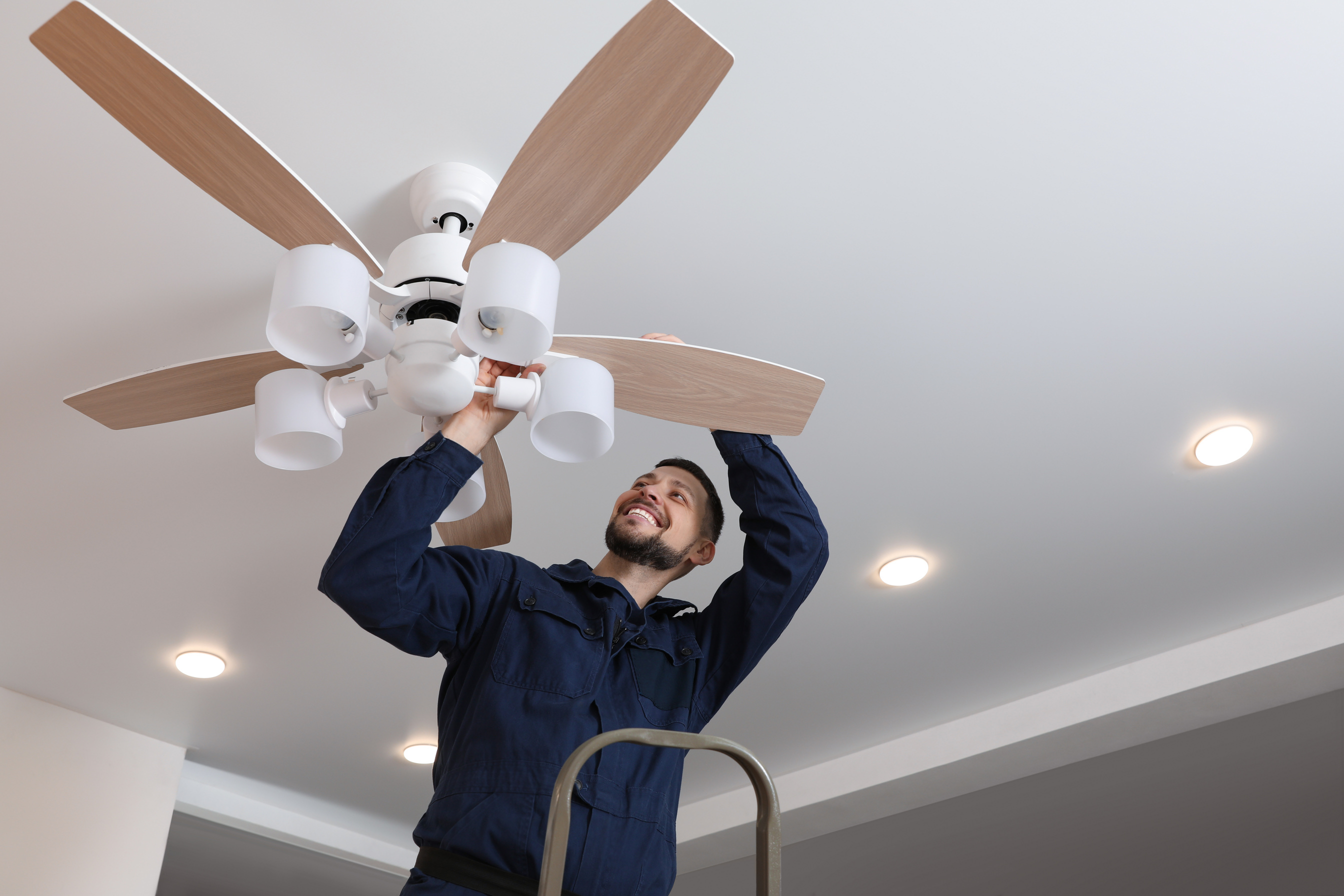 Electrician Repairing Ceiling Fan with Lamps Indoors